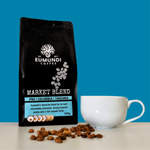 Eumundi Coffee market blend coffee bean bag with coffee beans and coffee cup on table.