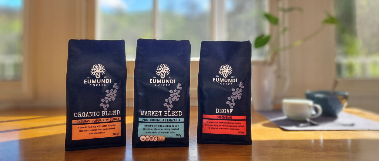 Eumundi Coffee retail bags of coffee on a kitchen table. Breakfast bowl and coffee cup in background.